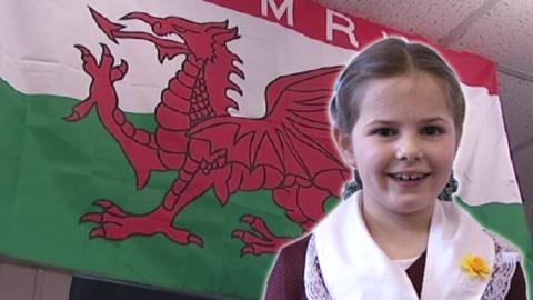 A young girl smiling in front of the Welsh flag