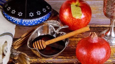 Images shows items on a table including a horn, an apple and some honey.