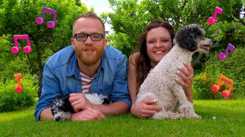 Ferne and Rory lay on their stomachs on the grass holding a dog each.