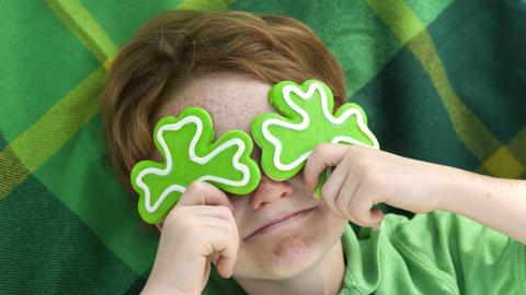 A young boy hold foam green shamrocks over his eyes.