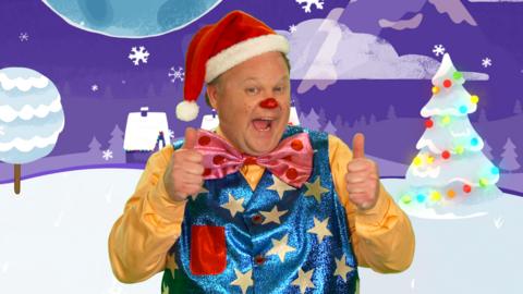 Mr Tumble wearing a Father Christmas hat, thumbs up smiling.