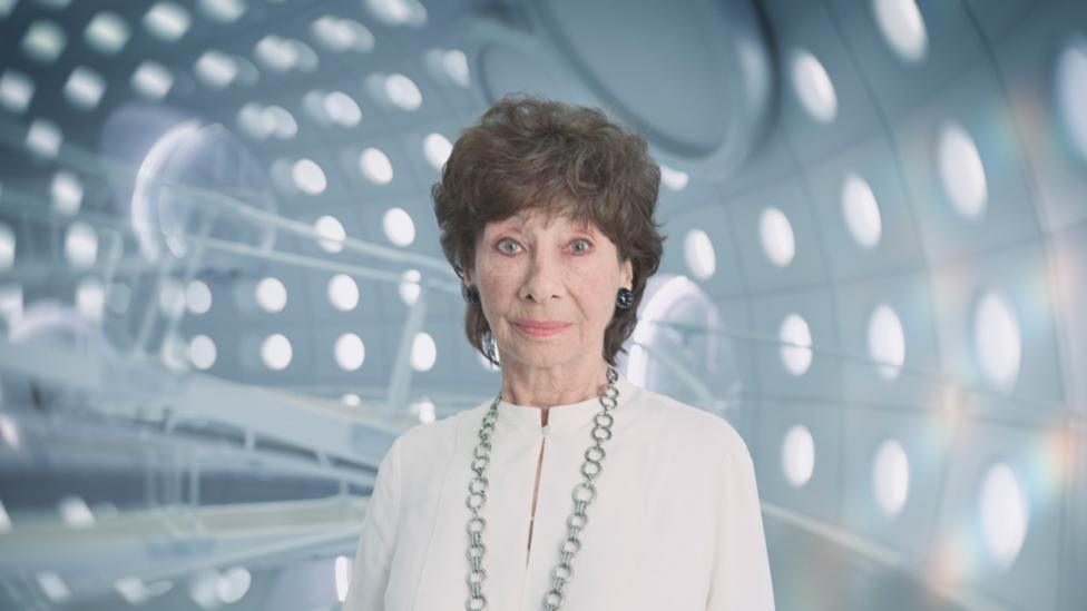 Susan Foreman, The Doctor's granddaughter, she is an older woman with brown hair, standing inside the TARDIS.