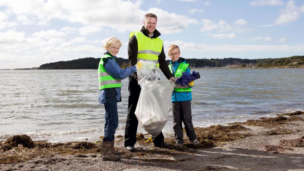 Two boys and a man cleaning up litter on a beach.