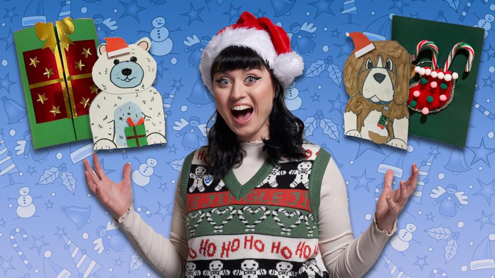 Abby from Blue Peter sits in a Christmas jumper and Santa hat with her arms open and mouth looking shocked. There are two christmas cards above her left hand and two above her right.