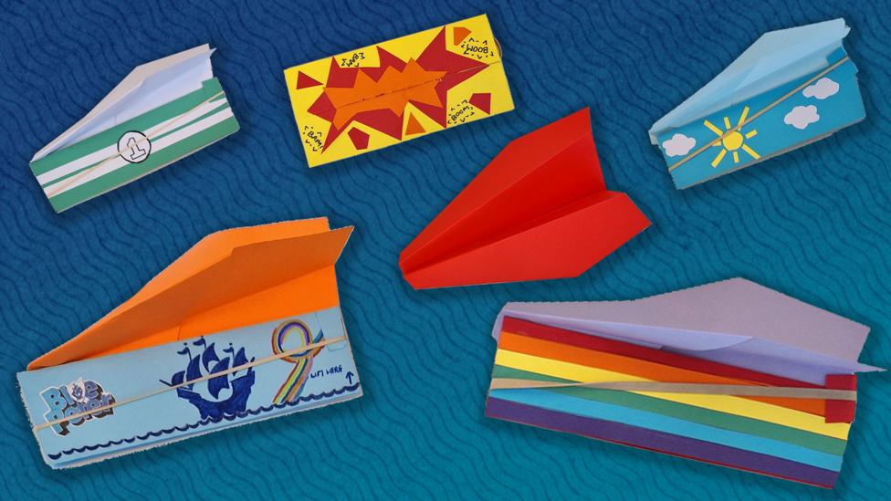 A collection of different colour paper planes, some have a rainbow pattern, a race car pattern, and a variety of other colourful patterns.