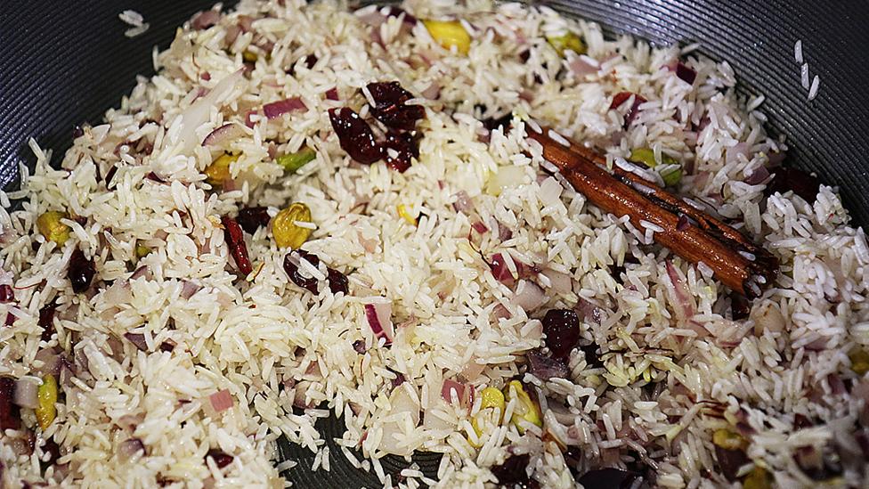 Cinnamon sticks, pistachios, cranberries and onions in a pan.