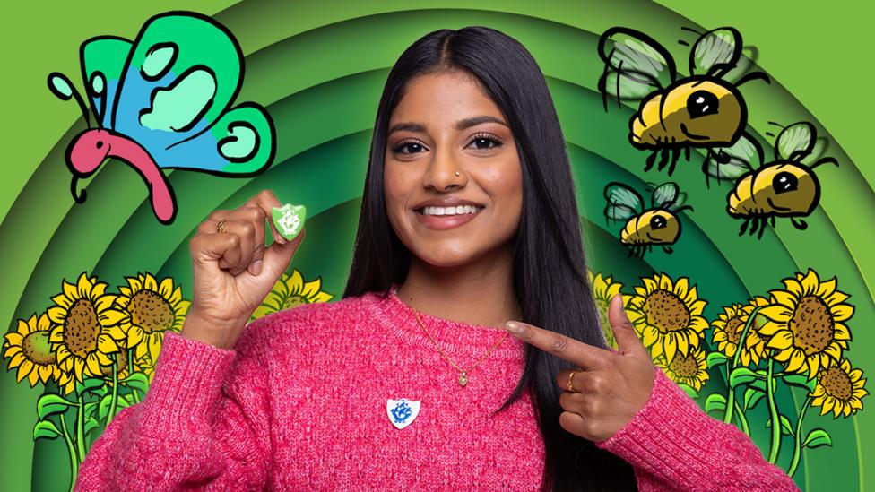 Blue Peter's Shini is holding a Green Blue Peter badge and pointing to it. On the background behind her are sunflowers, bees and a butterfly.