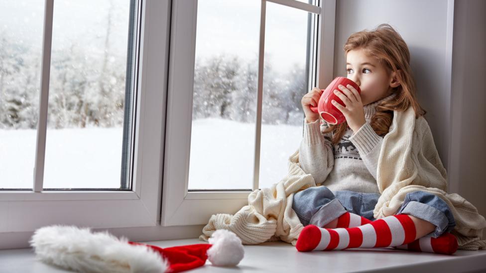 Girl sitting by window drinking out of Christmas mug