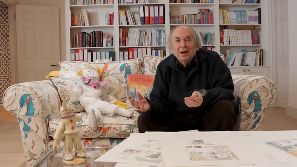 An old man sitting on a sofa holding a children's book