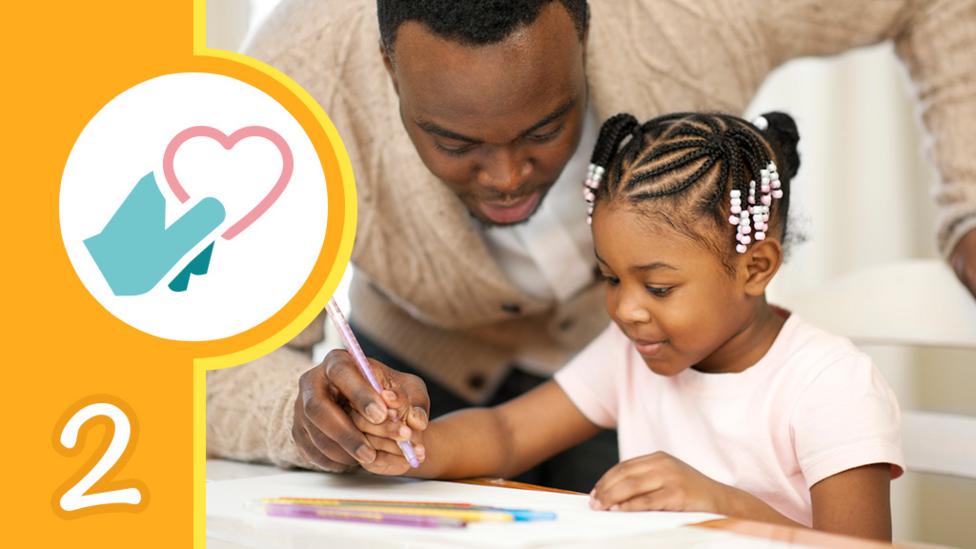 Father looking over his daughters shoulder while she colours in a picture