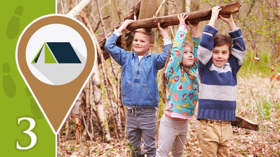 Three children picking up a log in a woodland