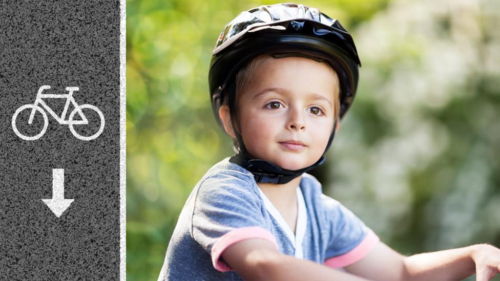 Close up of a little boy wearing a cycling helmet and resting his hands on the bike handle bars