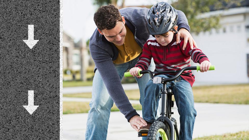 Little boy on a bike and his father is helping him put his feet on the pedals