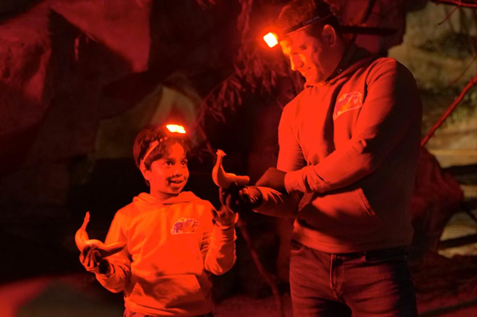 Steve and Aneeshwar are stood next to one another in a dark cave, wearing headlamps illuminating them in red.