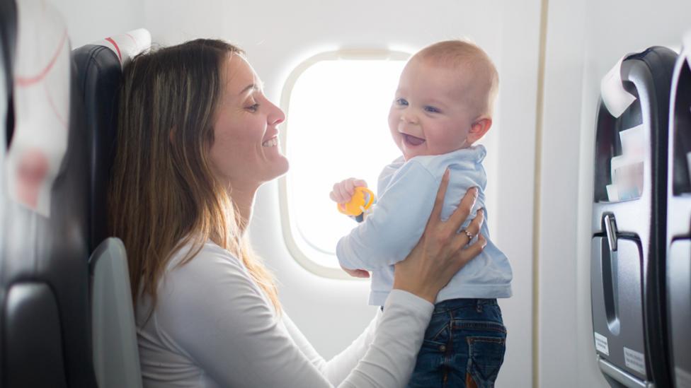 A mother holding her baby in front of her face, smiling, while sat on a plane.