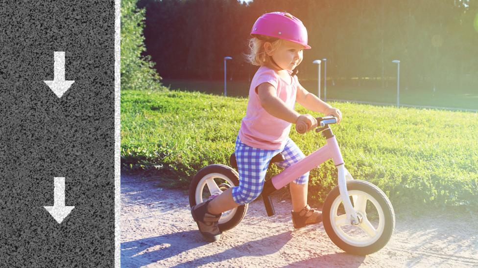 A little girl on her bike pushing herself along with her feet