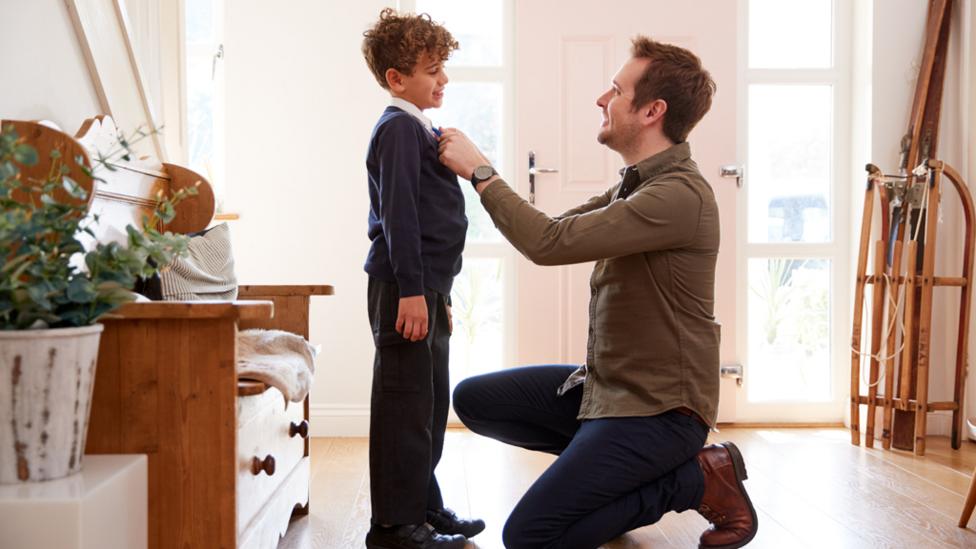 A father knelt in front of his young son, helping his with his school uniform.