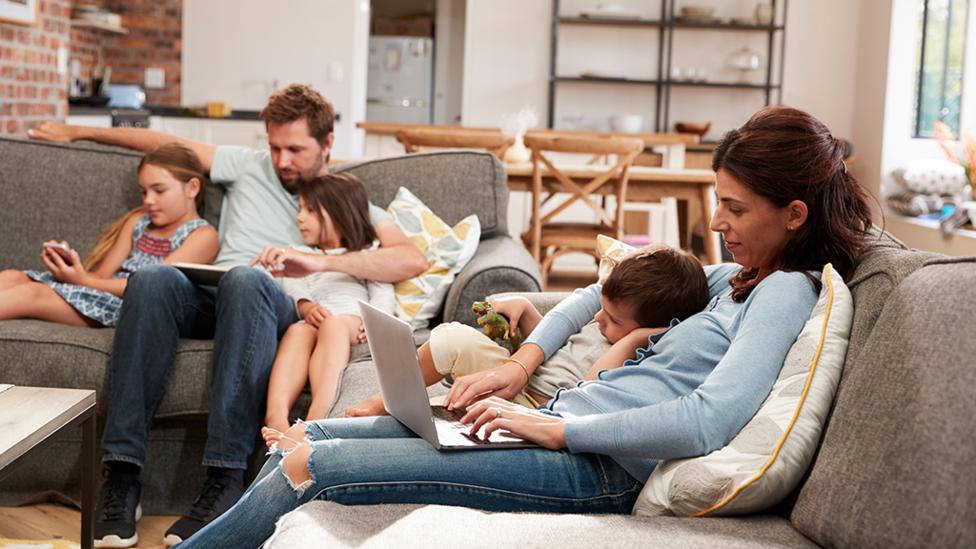 A family sitting on a sofa playing with their devices.