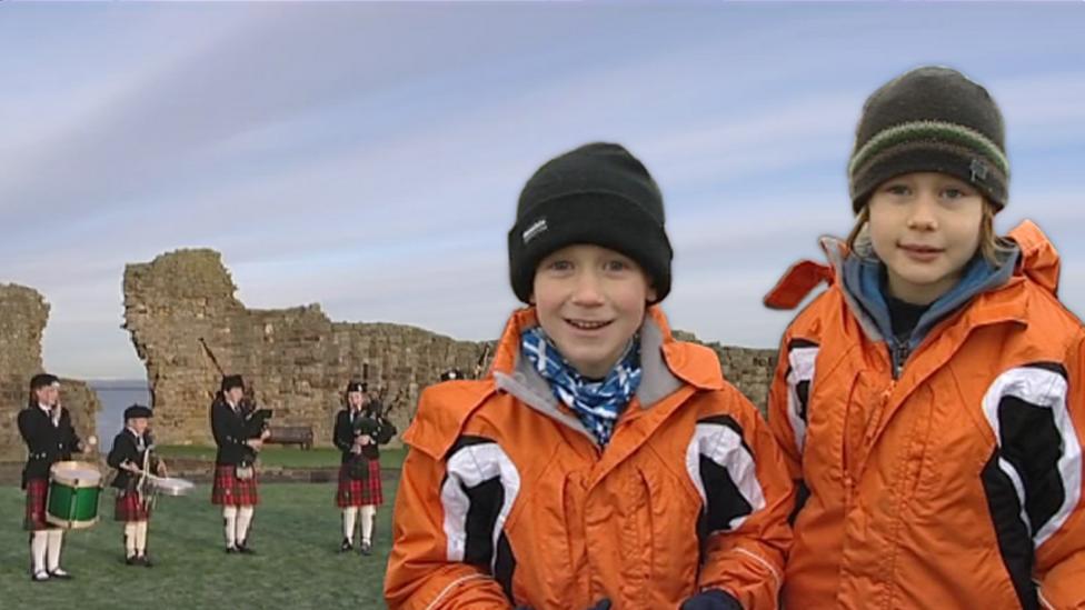 Two young boys standing in front of a traditional Scottish band