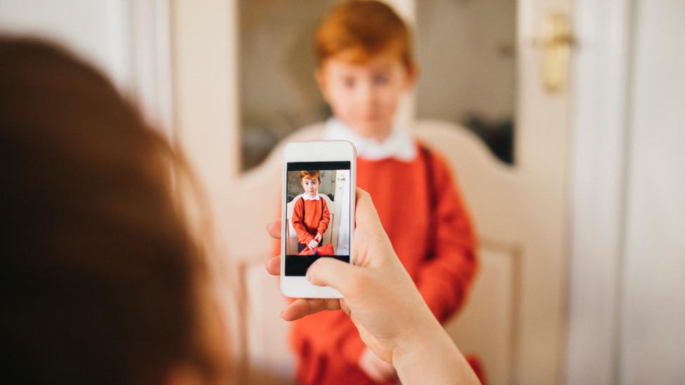 Parent taking a picture of her son. Son blurred in background, phone in focus.