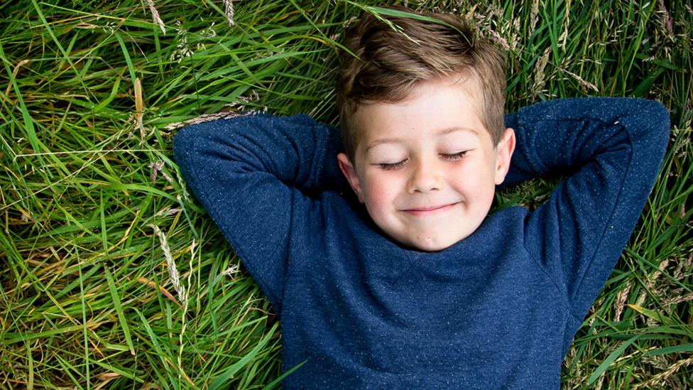 A young boy lying on the grass with his eyes closed looking happy.