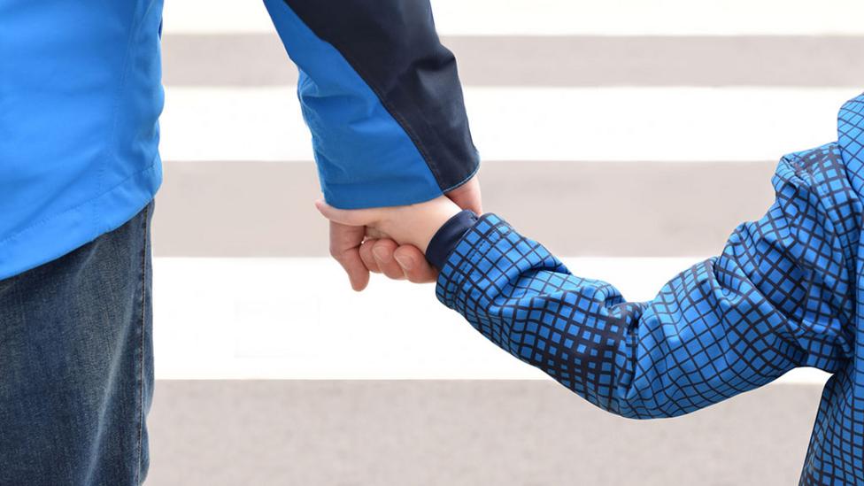 A parent and child holding hands as they cross the road.