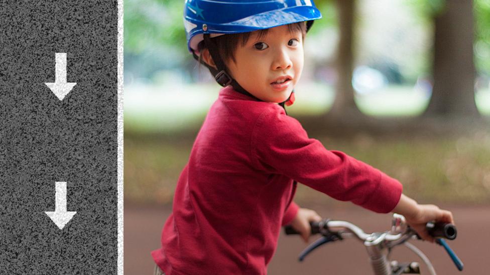 Little boy sat on a bike with his head turned so that he is looking at the camera