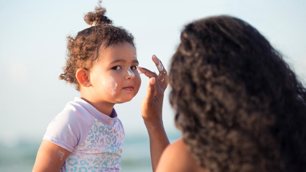 Young girl having suncream applied by her mother.