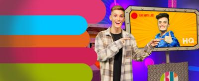 Lee on CBBC HQ set pointing to the TV screen with Joe live inside.