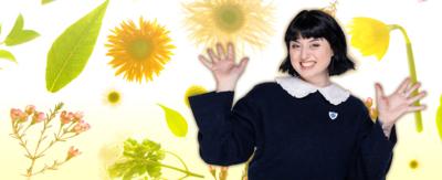 Blue Peter presenter Abby is smiling with her arms up by her face. On the background is a selection of different flowers and leaves.