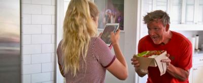 Gordon Ramsay smiles while holding a box of LA Nachos, Tilly takes a picture of him using her tablet.