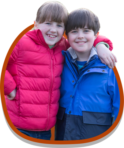 A young boy and girl are smiling with their arms on each others shoulders.
