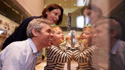 Mother, Father and a young child are looking through a glass window in a museum.