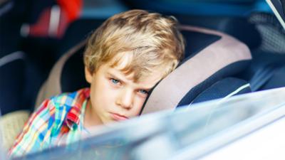 A young boy looking bored sat in a car seat with the window rolled down.