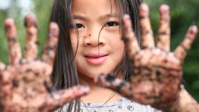 Young girl with her muddy hands held up to camera.
