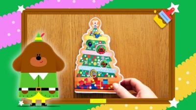 Hey Duggee in his elf costume next to a Christmas tree make.