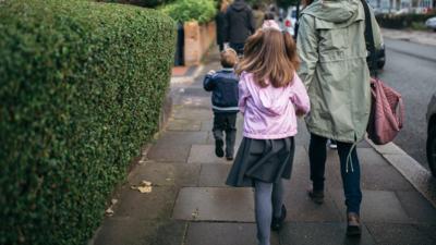 Children walking to school holding their parents hand.