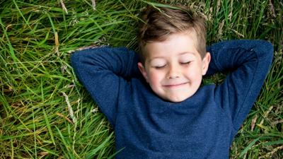 A young boy lying on the grass with his eyes closed looking happy.