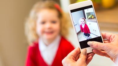 A little girl wearing a plain school uniform having her picture taken with a mobile phone.