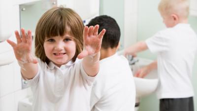 Young boy with holding his soapy hands up, two young boys washing their hands in the background.