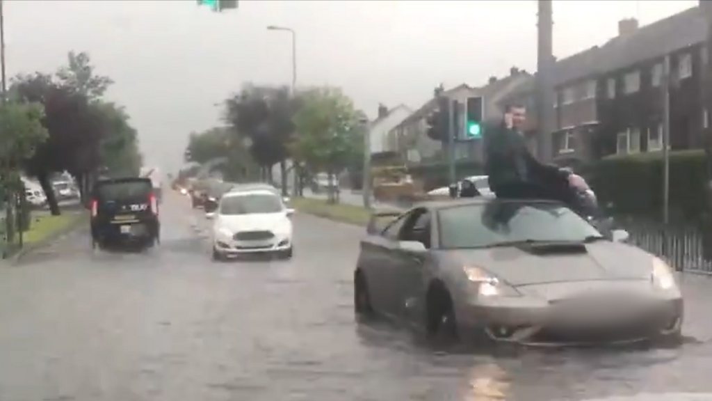 A man was filmed sitting on top of a car during the flooding.