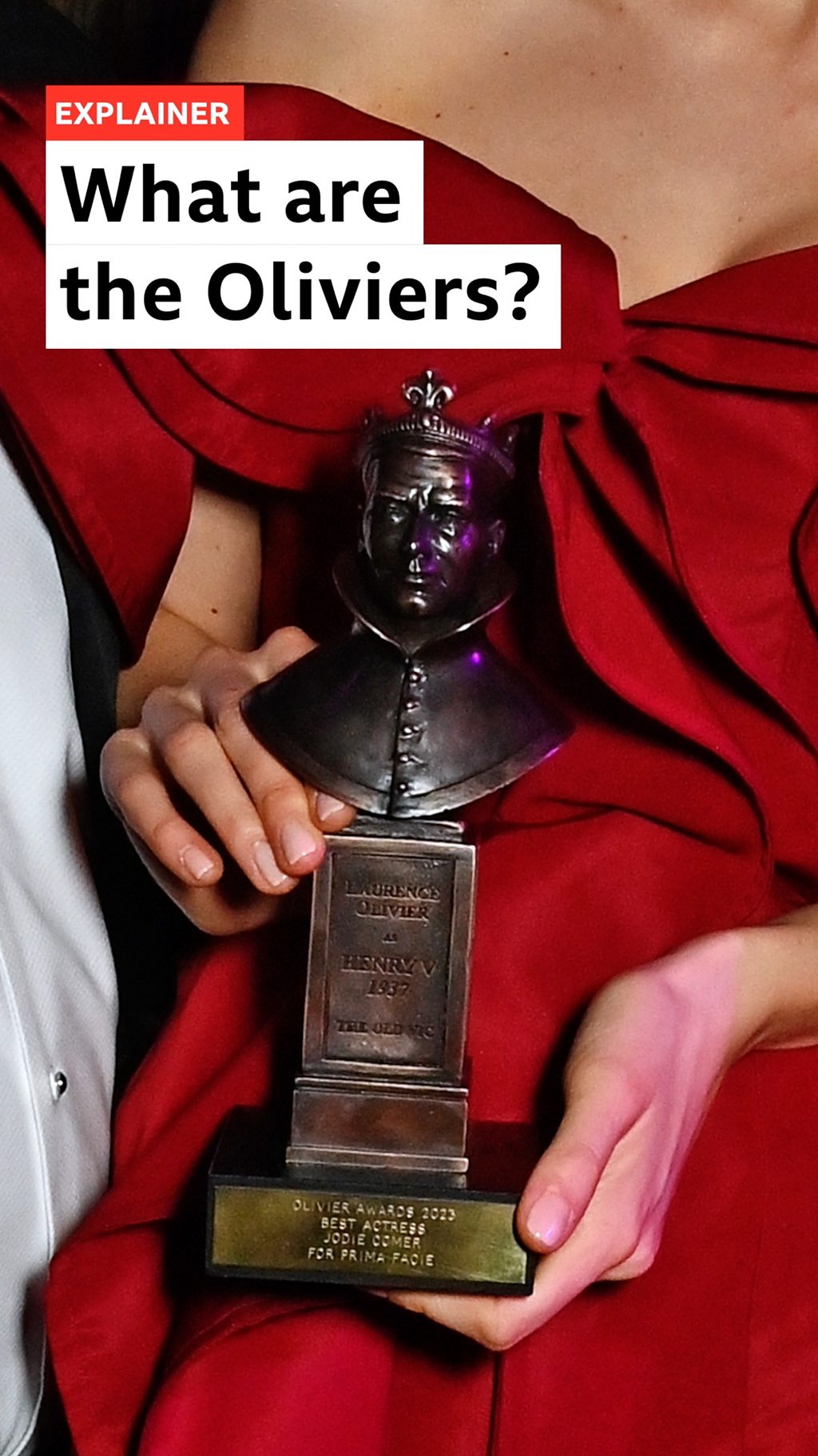 An Olivier Award trophy held by two hands in front of a red dress