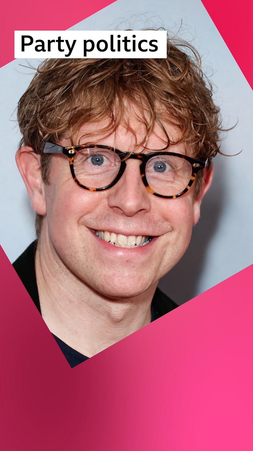 A man, Josh Widdicombe, smiles - he has wavy brown hair and wears dark round glasses