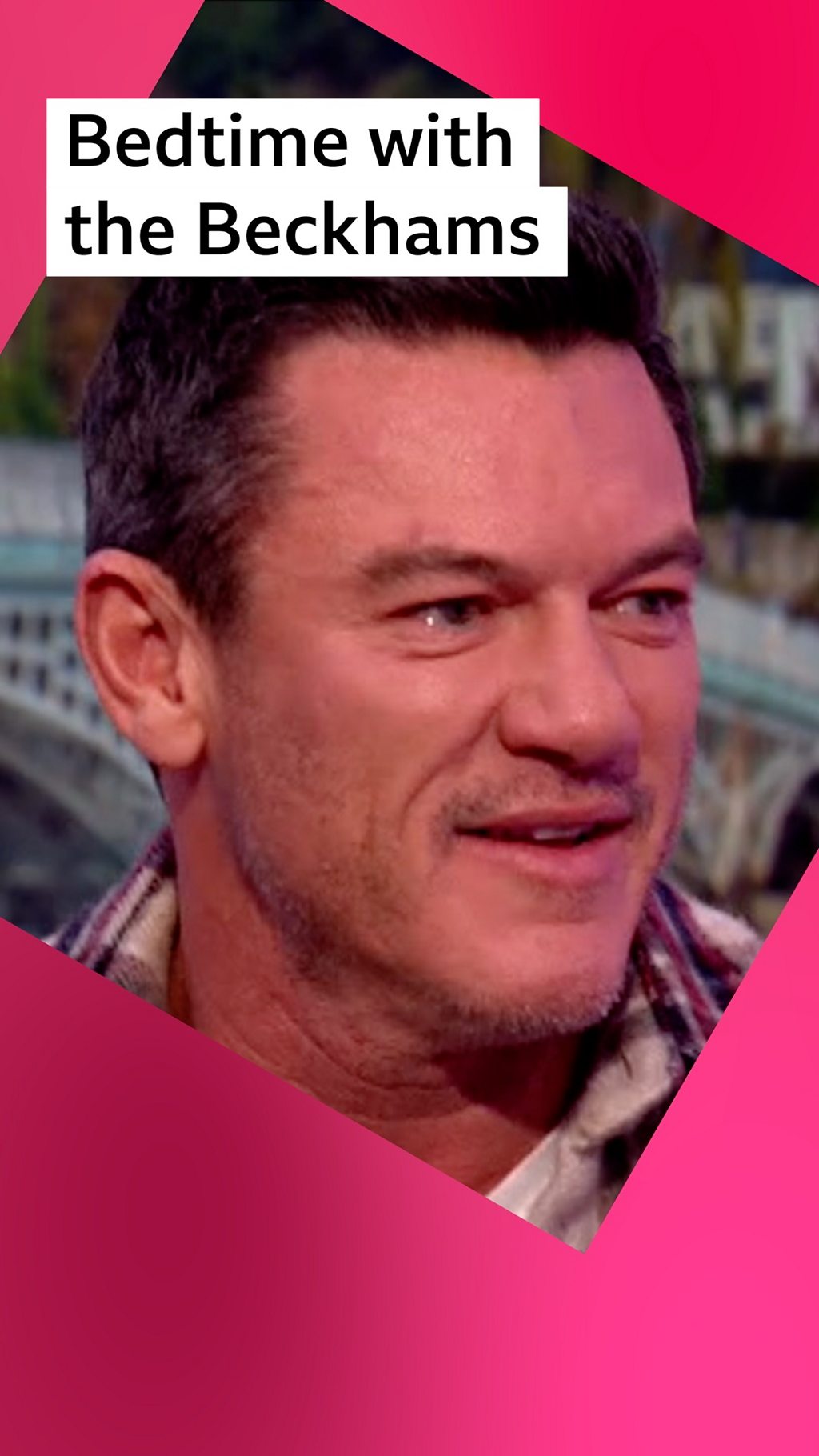 A man, Luke Evans is smiling, onscreen text reads: "Bedime with the Beckhams"