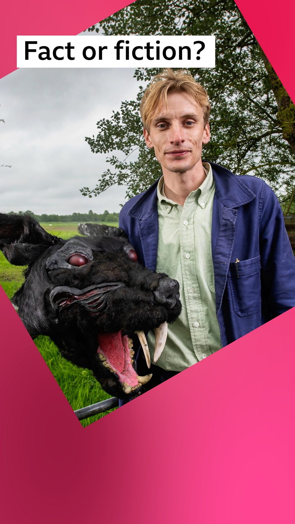 A man, Charlie Cooper, stands in a field, with a recreation of a black dog's head with red eyes and sharp fangs