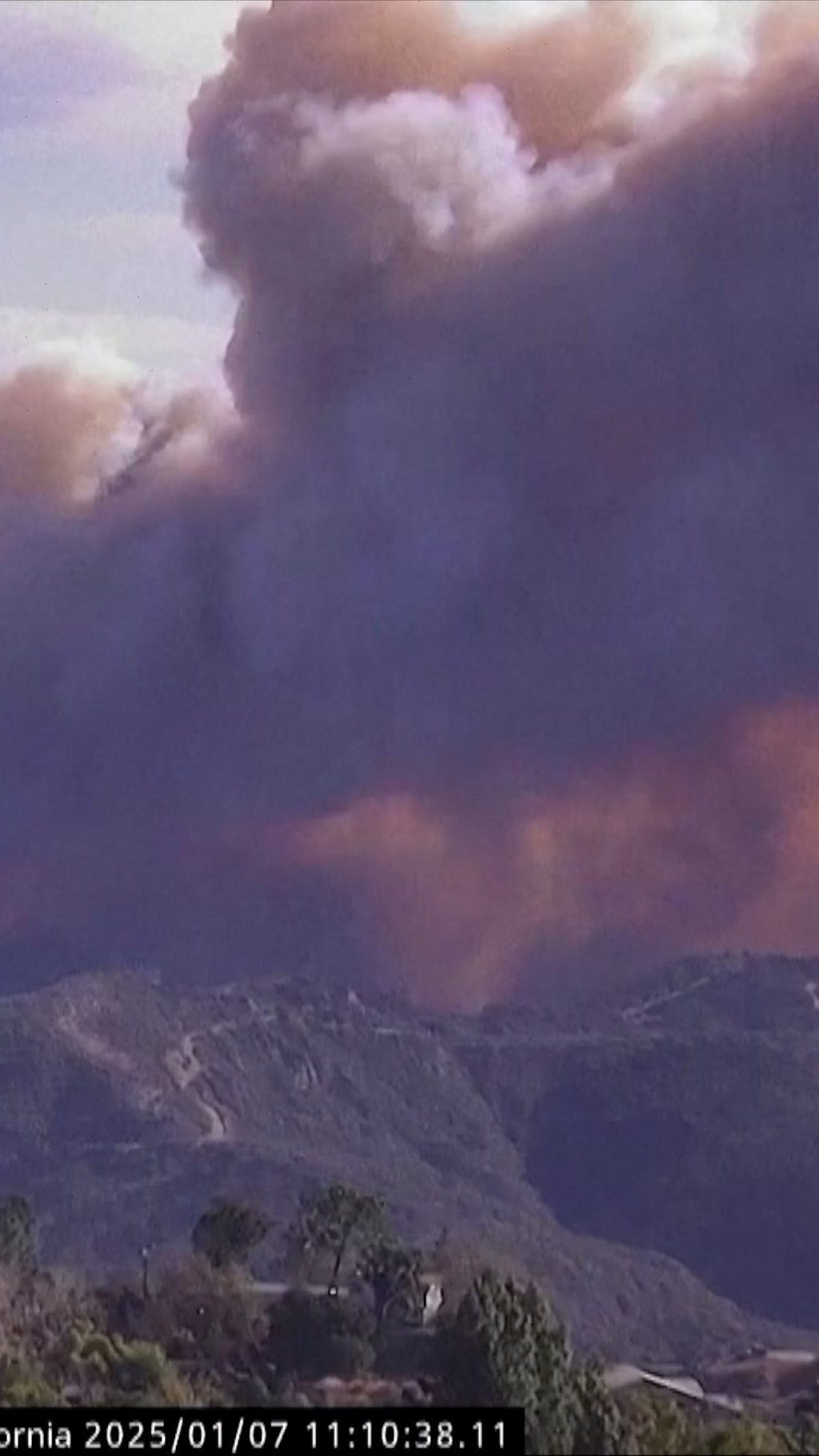 A vertical image of smoke billowing over hills in LA