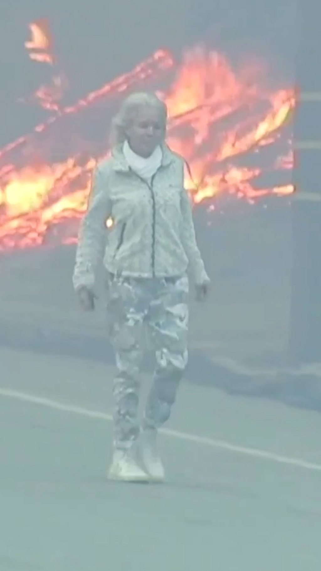 A woman walking down a road with flames in the background