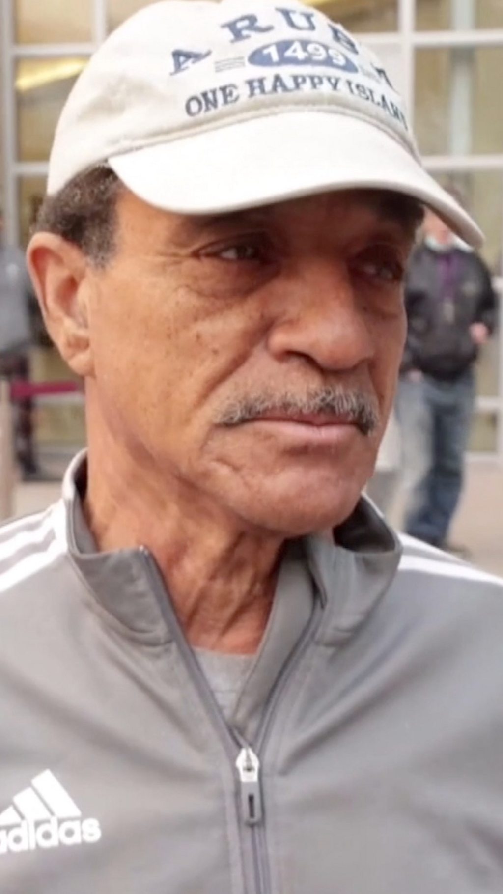 A man in a white cap looks solemnly out of frame