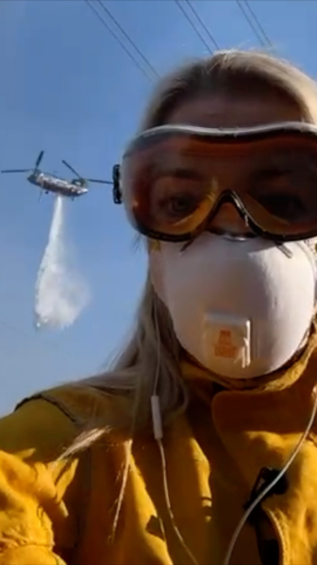 Emma Vardy in a mask an goggles, a helicopter is dumping water behind her