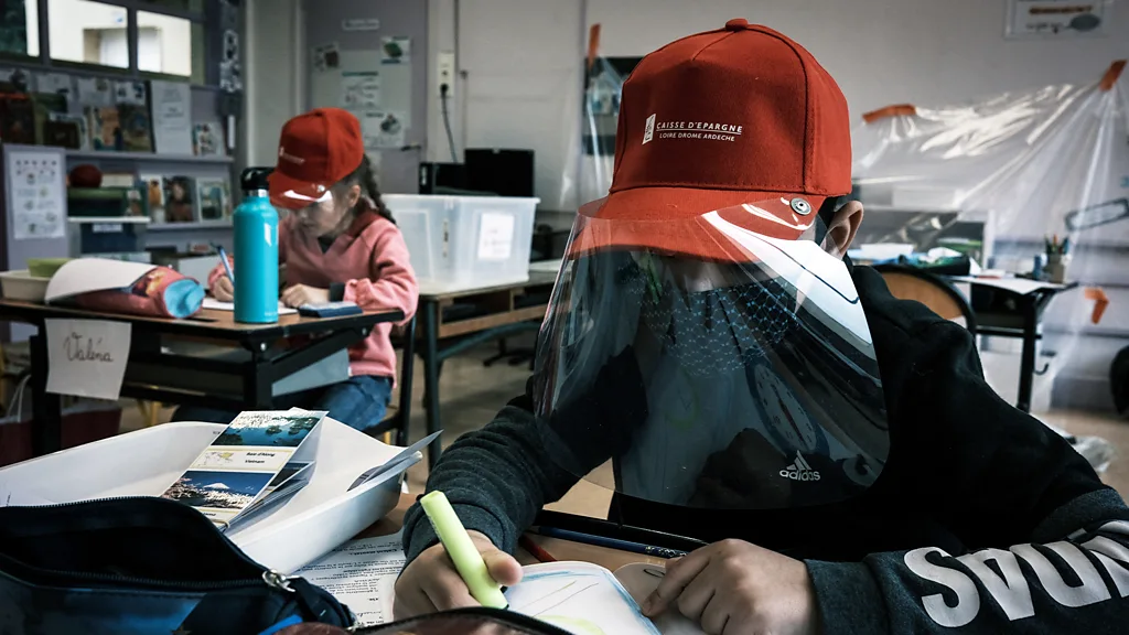 Two students wear red hats with visors in front of them, in class